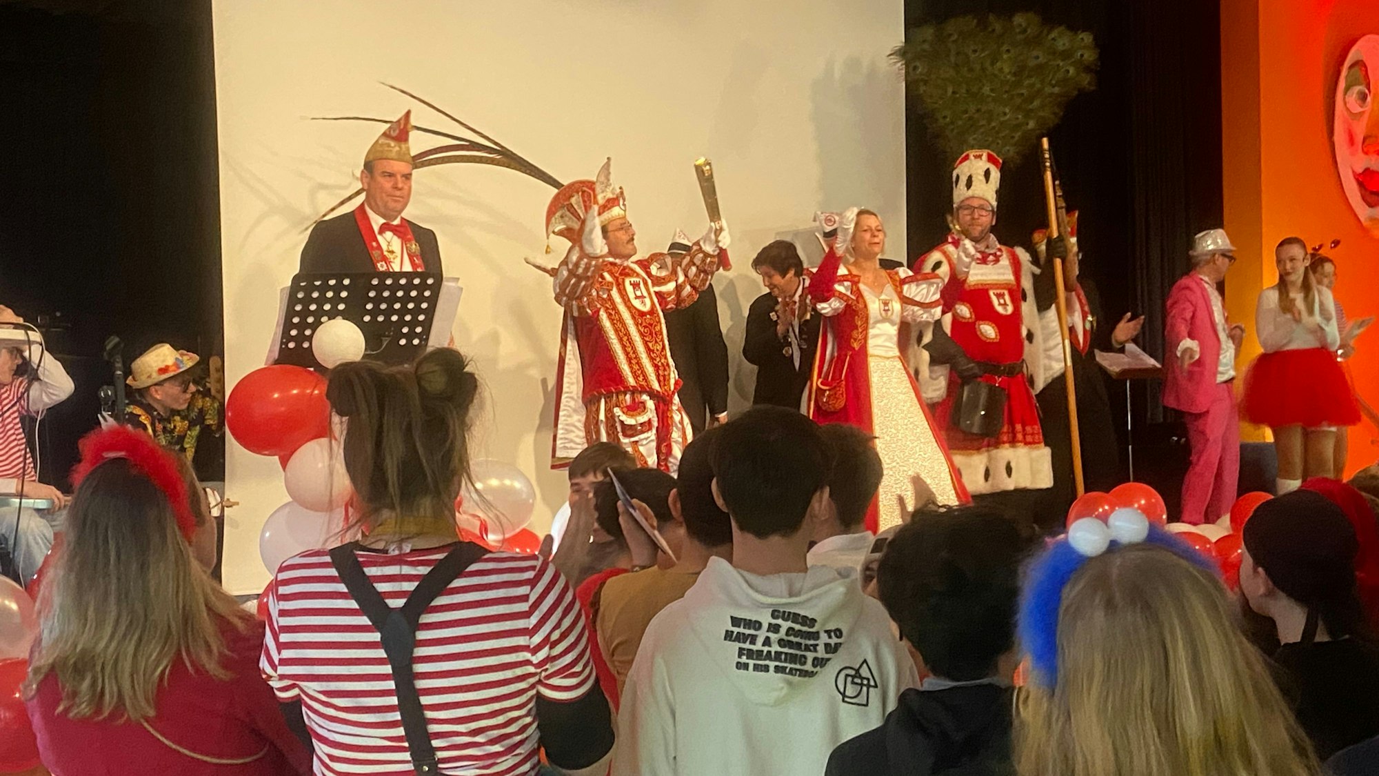 Das Porzer Dreigestirn in der Aula des Stadtgymnasium Köln-Porz mit bunt kostümierten Jecken.