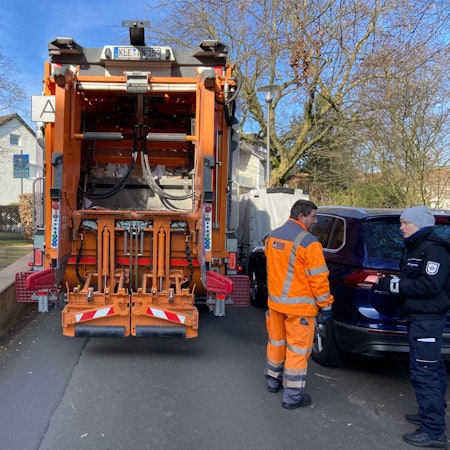 Ein Müllauto steht auf einer Straße zwischen einer Grundstücksmauer und geparkten Fahrzeugen ist kaum ein Durchkommen.