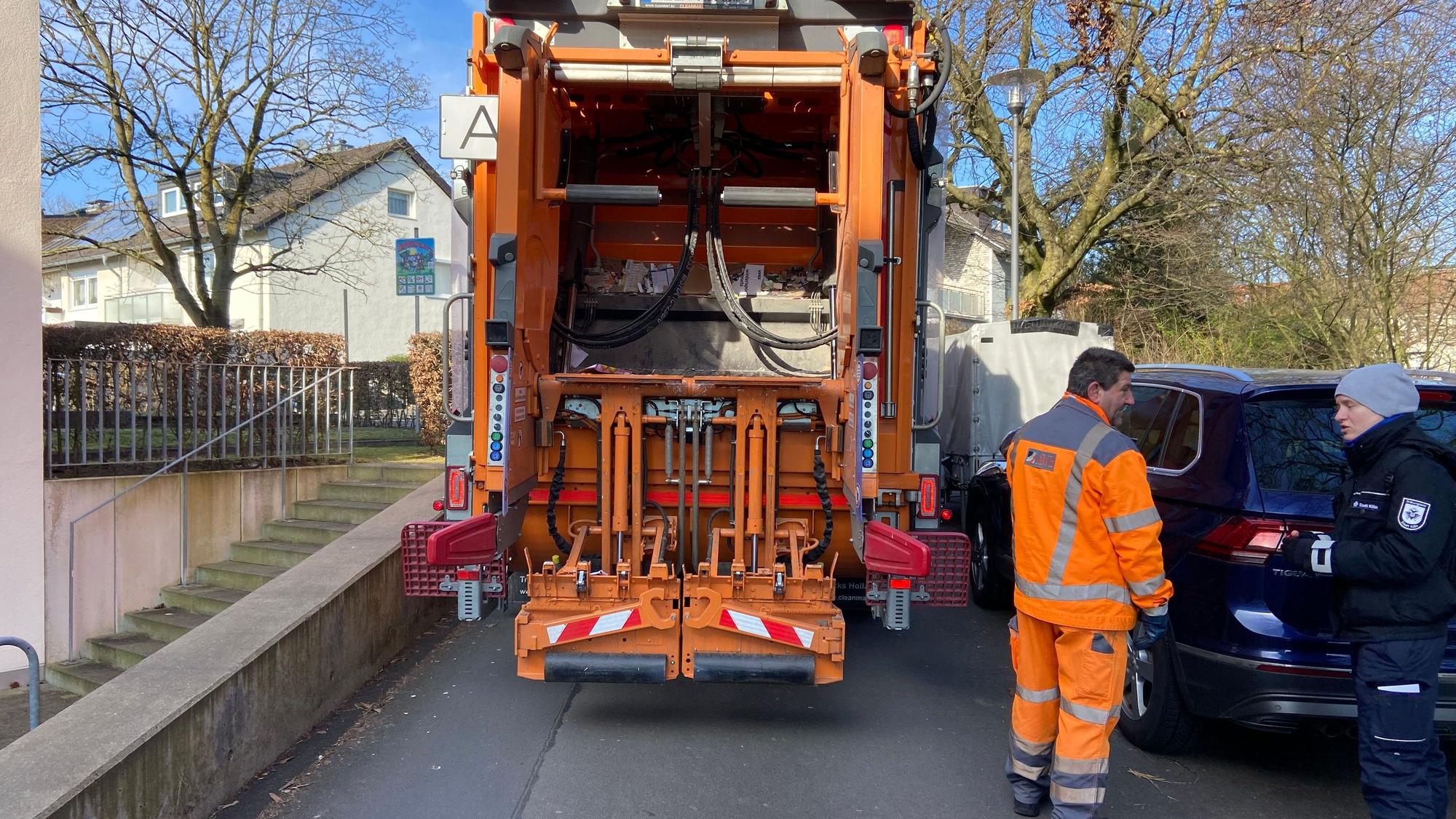 Ein Müllauto steht auf einer Straße zwischen einer Grundstücksmauer und geparkten Fahrzeugen ist kaum ein Durchkommen.