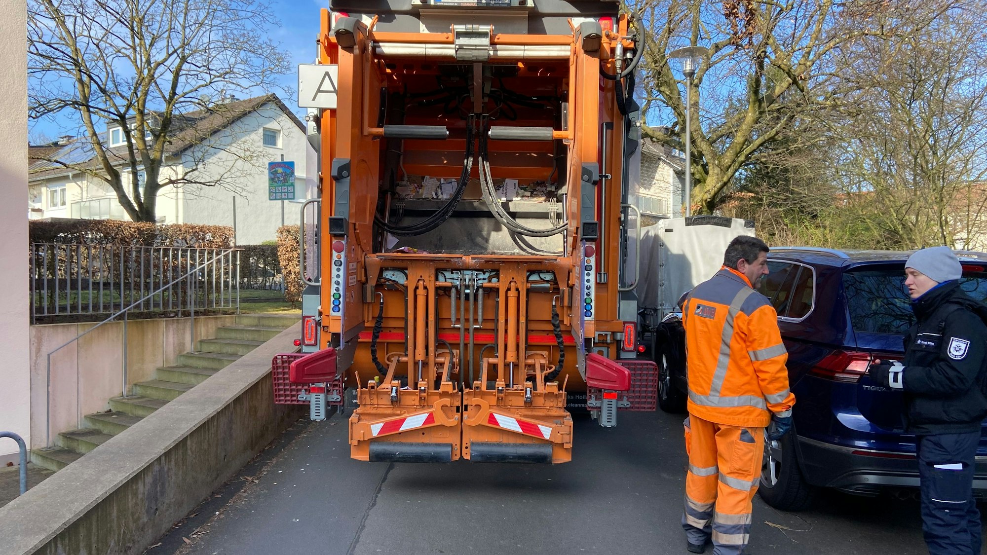 Ein Müllauto steht auf einer Straße zwischen einer Grundstücksmauer und geparkten Fahrzeugen ist kaum ein Durchkommen.