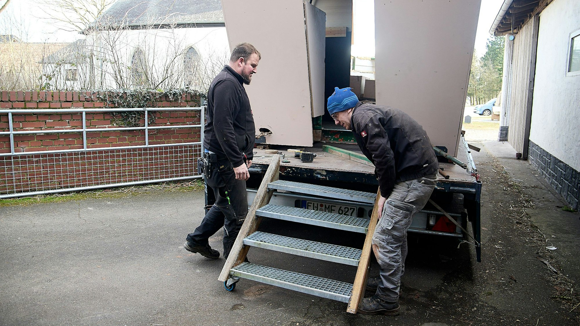 Zwei Männer stehen an einem Karnevalswagen und montieren eine Treppe.