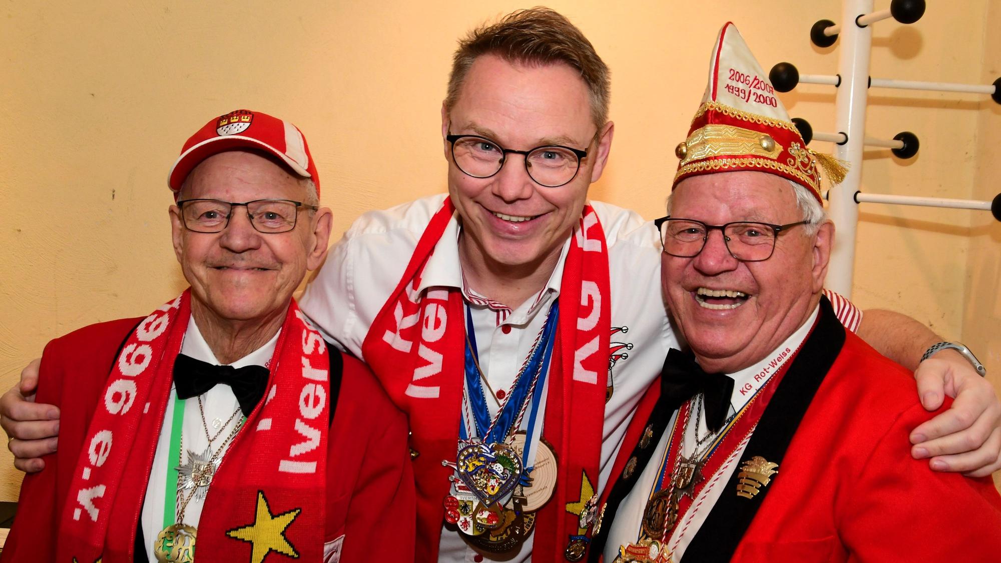 Drei Männer stehen Arm in Arm und lachen in die Kamera.