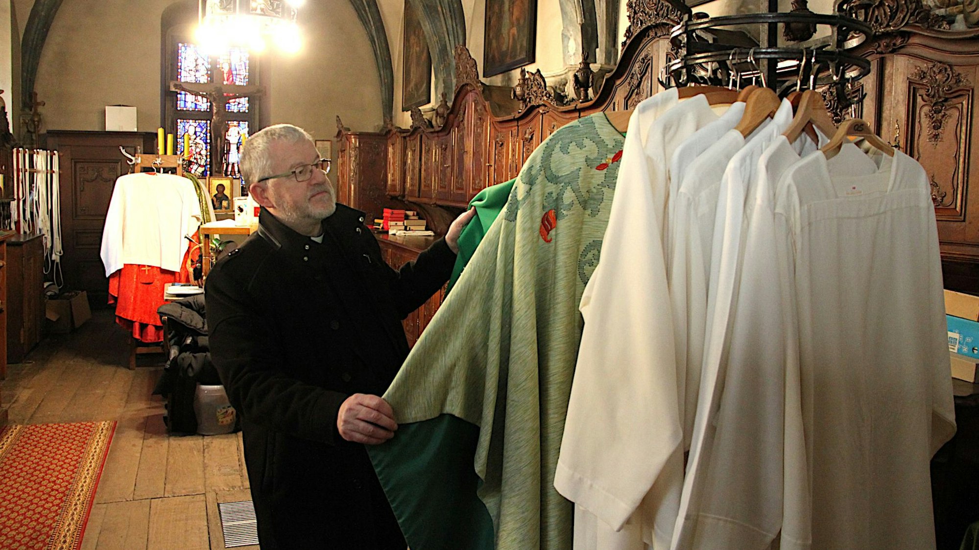 Der Steinfelder Pfarrer Wieslaw Kaczor steht in der Sakristei der Basilika und schaut sich Messgewänder an.
