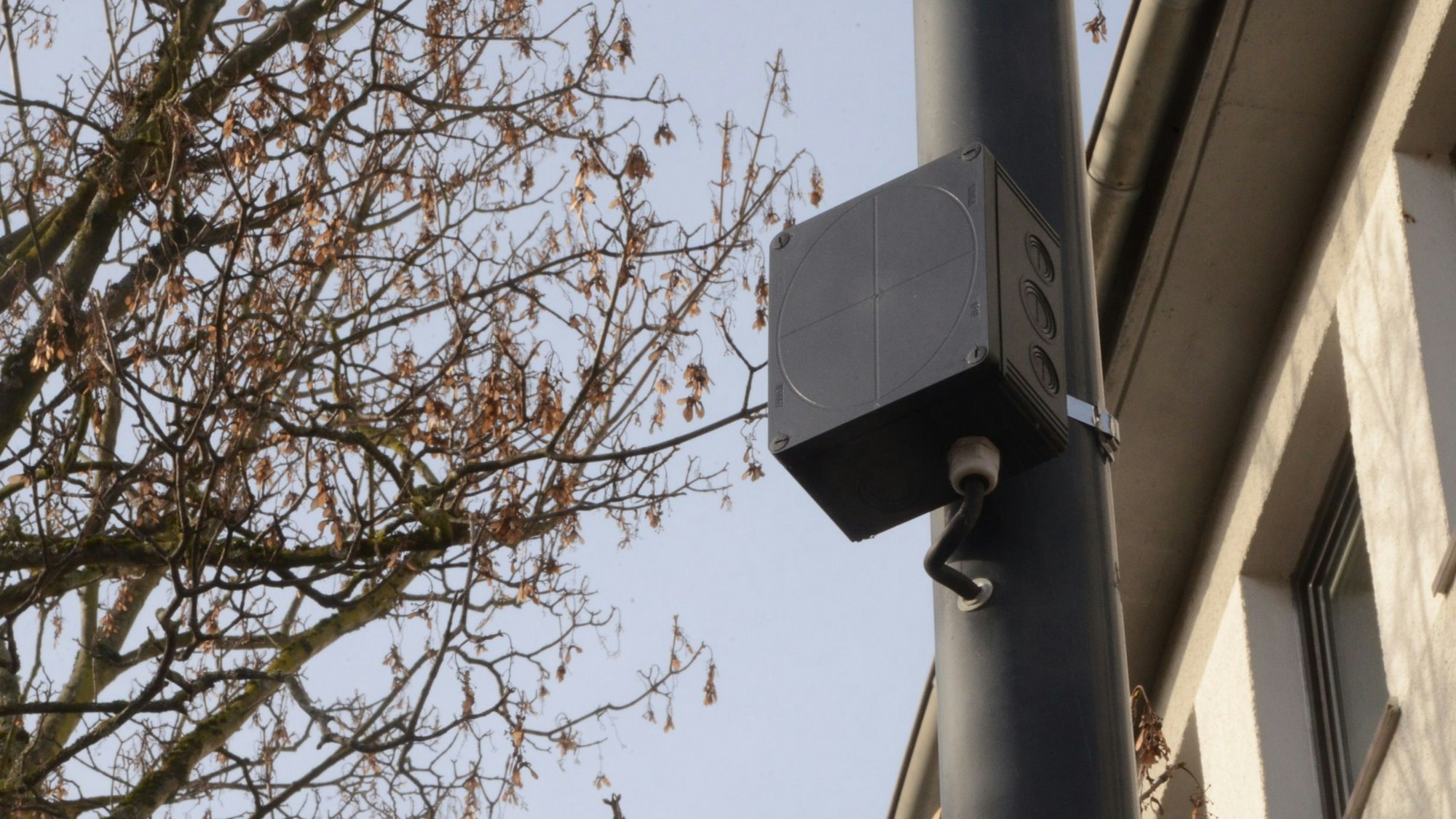 An einem Laternenmast ist ein kleiner schwarzer Kasten montiert.