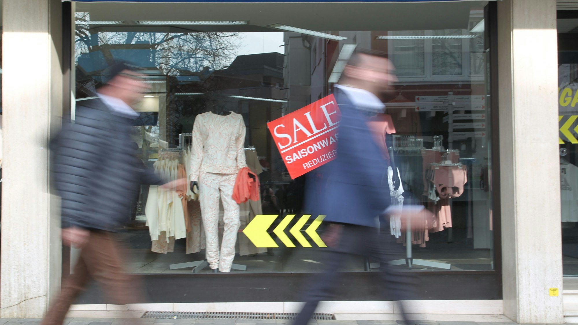 Zwei Männer gehen an einem Schaufenster vorbei.