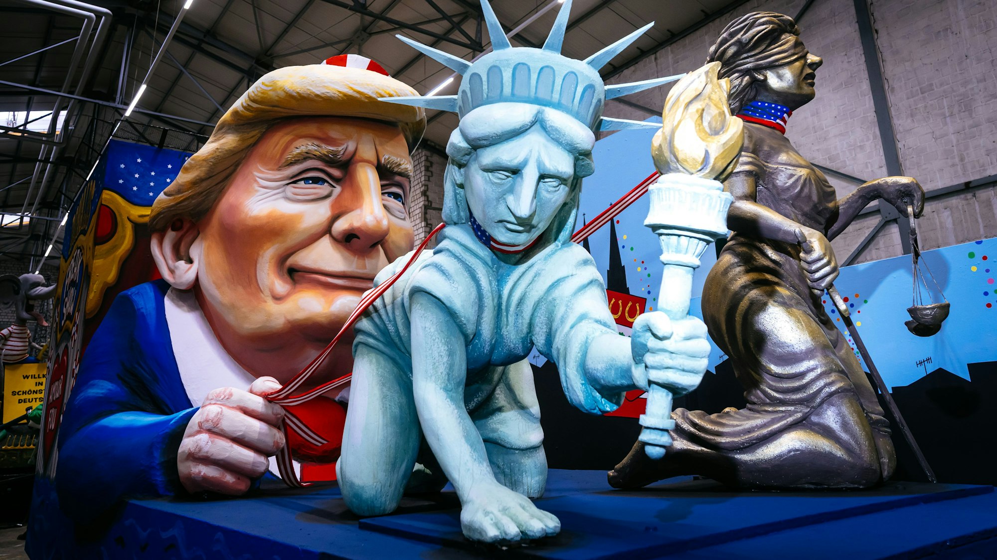 Donald Trump nimmt die Freiheitsstatue und Justicia, die Göttin der Gerechtigkeit, an die Kette.