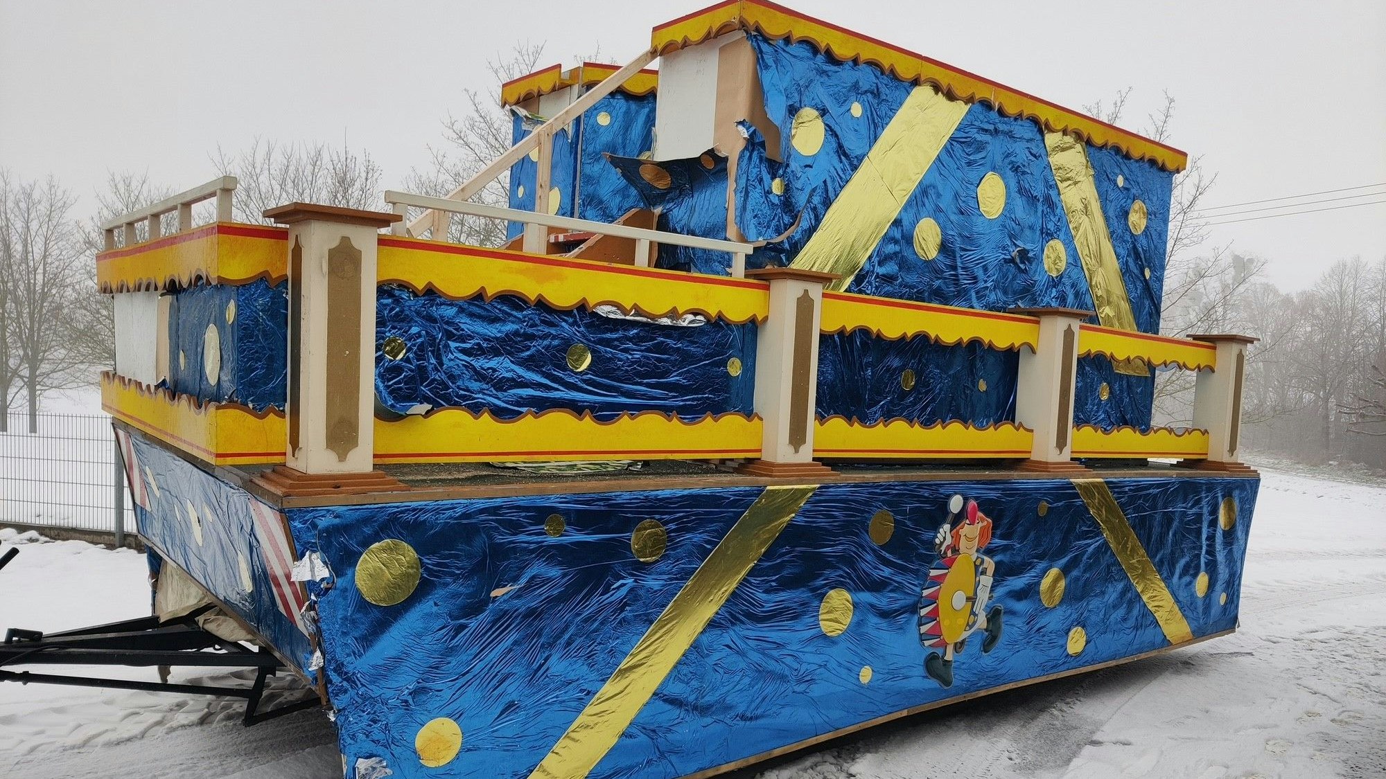 Ein mit blauer und goldener Folie geschmückter Karnevalswagen ist in einer verschneiten Landschaft abgestellt.