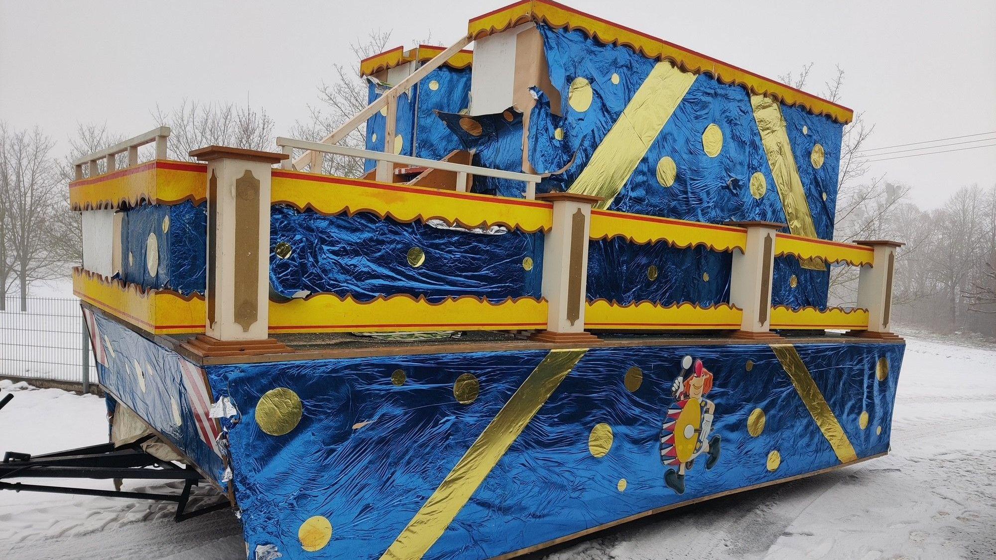 Ein mit blauer und goldener Folie geschmückter Karnevalswagen ist in einer verschneiten Landschaft abgestellt.