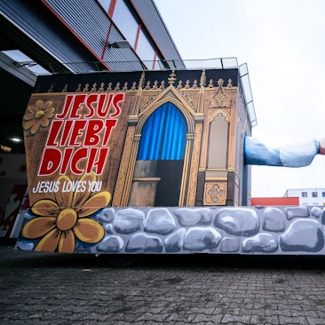 Der Persiflagewagen zum Thema Missbrauch in der Kirche steht beim Richtfest des Kölner Rosenmontagszuges in der Wagenhalle.