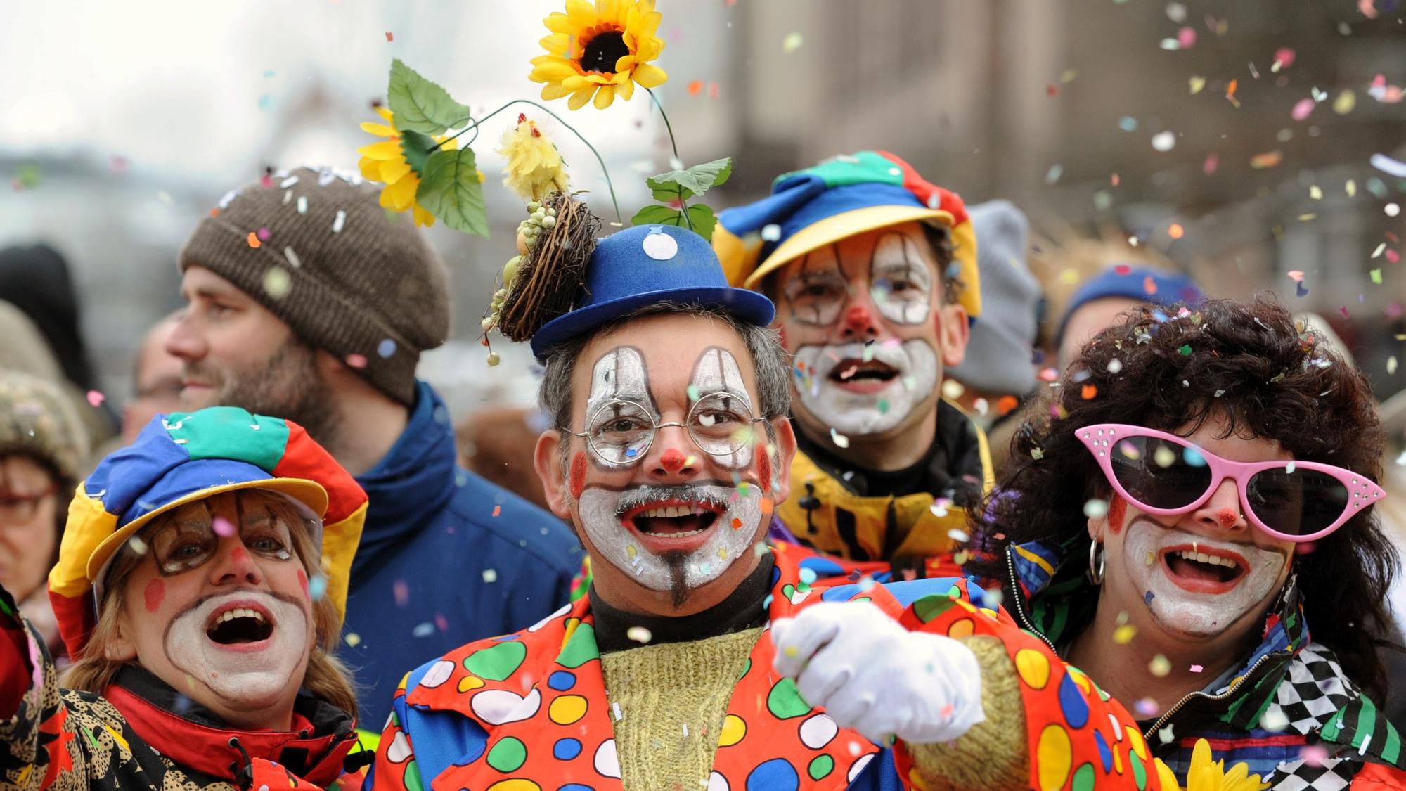 Besucher in Clown-Kostümen werfen bei einem Karnevalsumzug mit Konfetti.