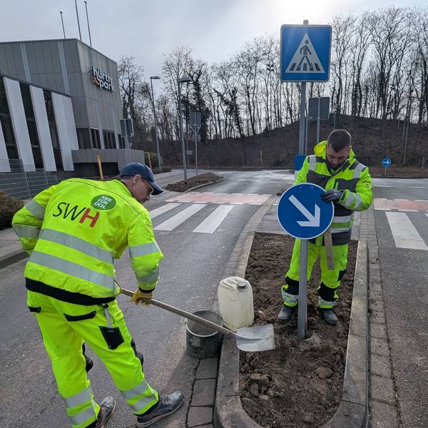 Das Foto zeigt zwei Mitarbeiter der Stadtwerke, die ein Verkehrsschild am Kreisverkehr aufstellen.