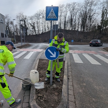 Das Foto zeigt zwei Mitarbeiter der Stadtwerke, die ein Verkehrsschild am Kreisverkehr aufstellen.