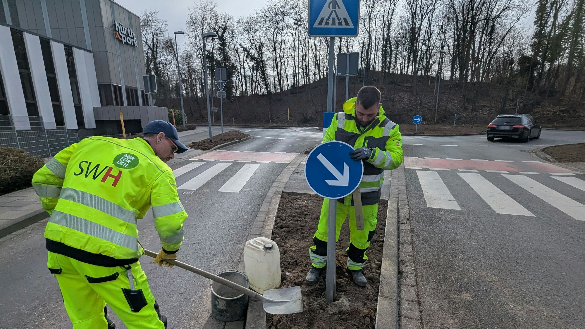 Das Foto zeigt zwei Mitarbeiter der Stadtwerke, die ein Verkehrsschild am Kreisverkehr aufstellen.