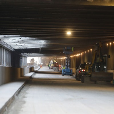 Blick in einen Tunnel, an dessen rechten Rand Baumaschinen und Fahrzeuge stehen.