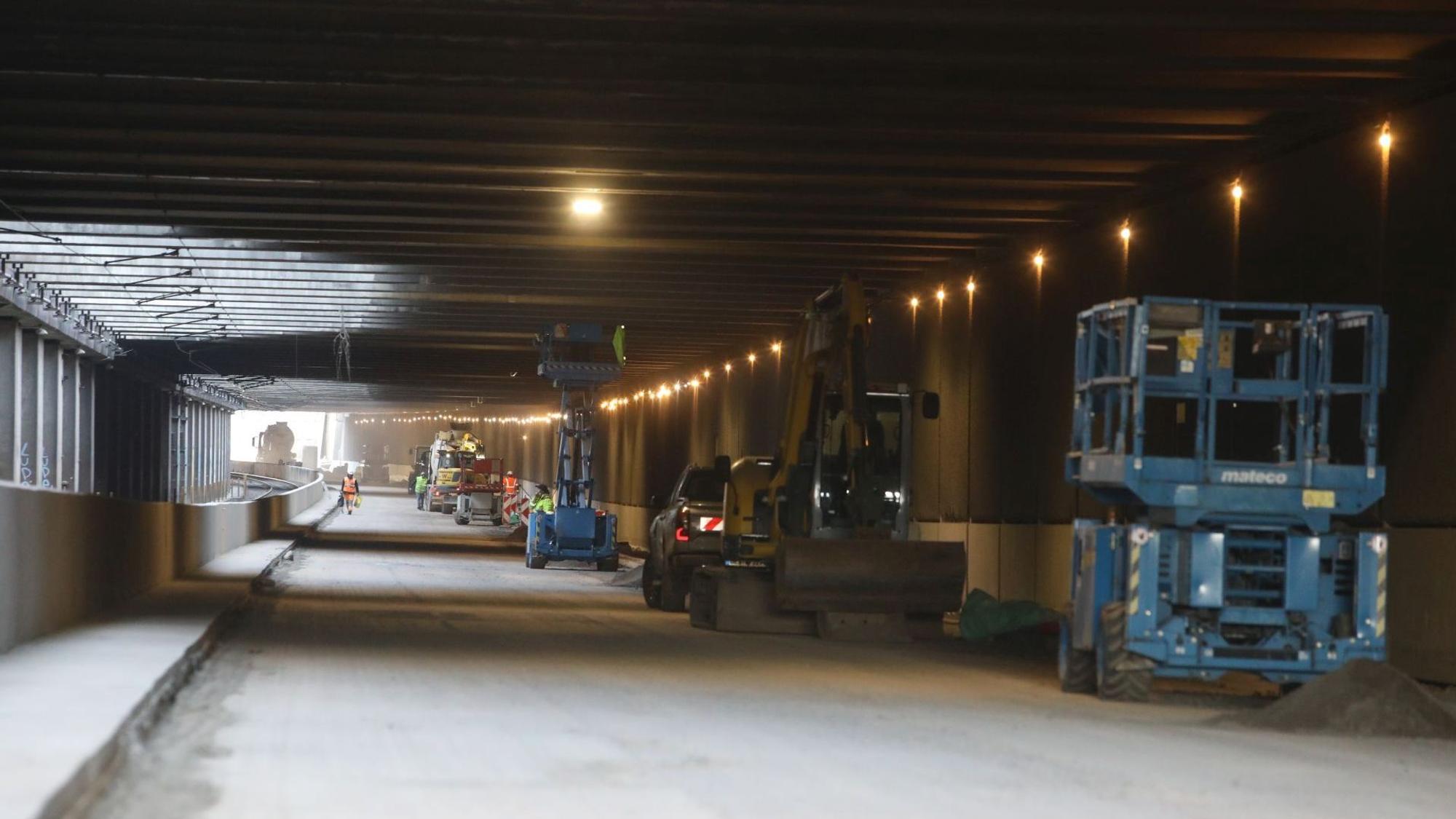 Blick in einen Tunnel, an dessen rechten Rand Baumaschinen und Fahrzeuge stehen.