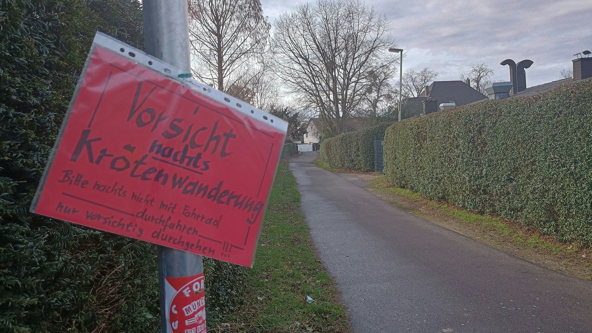 Auf dem roten Schild steht: „Vorsicht. Nachts Krötenwanderung. Bitte nachts nicht mit dem Fahrrad durchfahren. Nur vorsichtig durchgehen.“