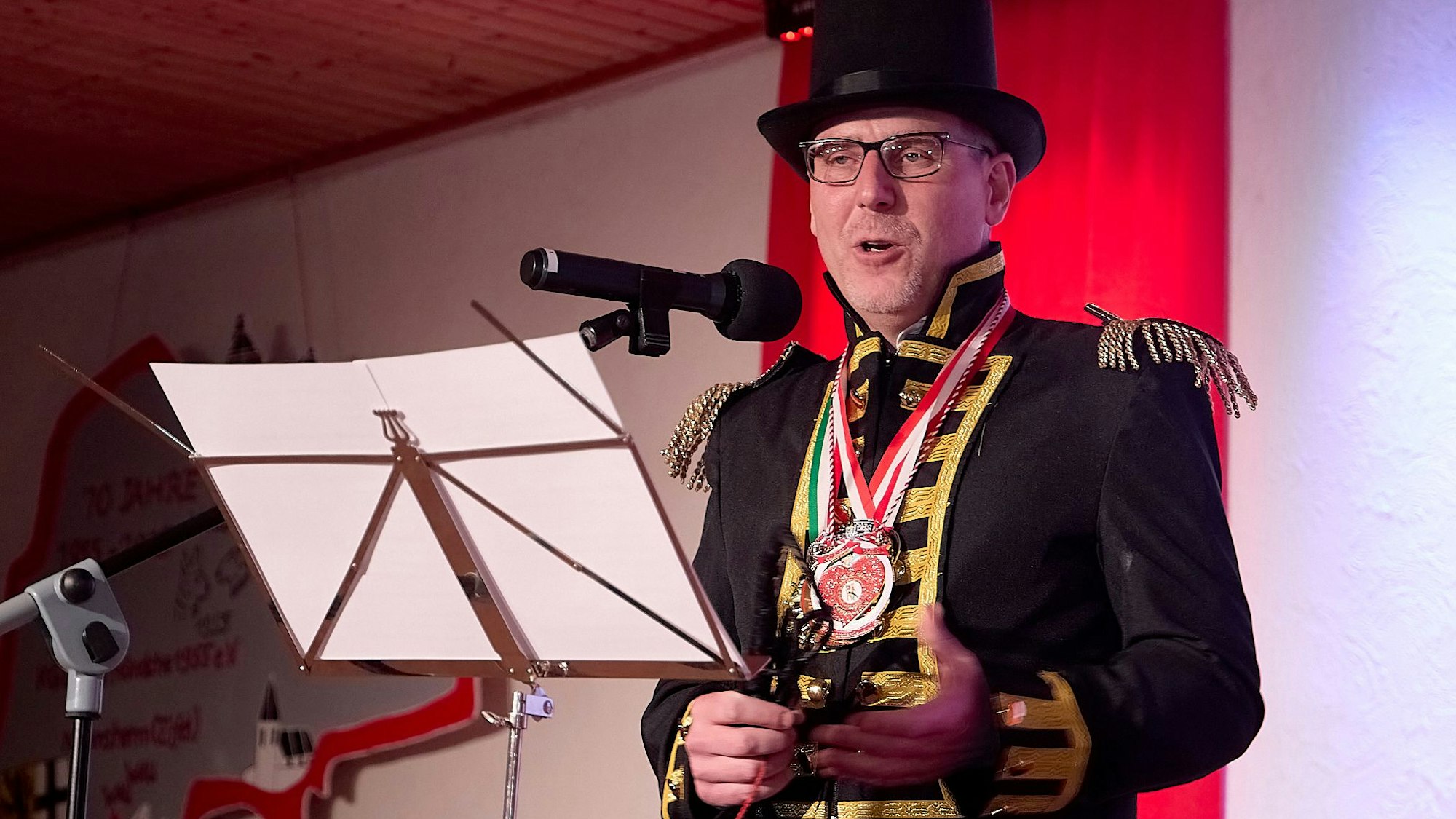 Nettersheims Bürgermeister Norbert Crump steht als Dompteur verkleidet an einem Notenständer, auf dem zwei Blätter sind. Er spricht in ein Mikrofon.