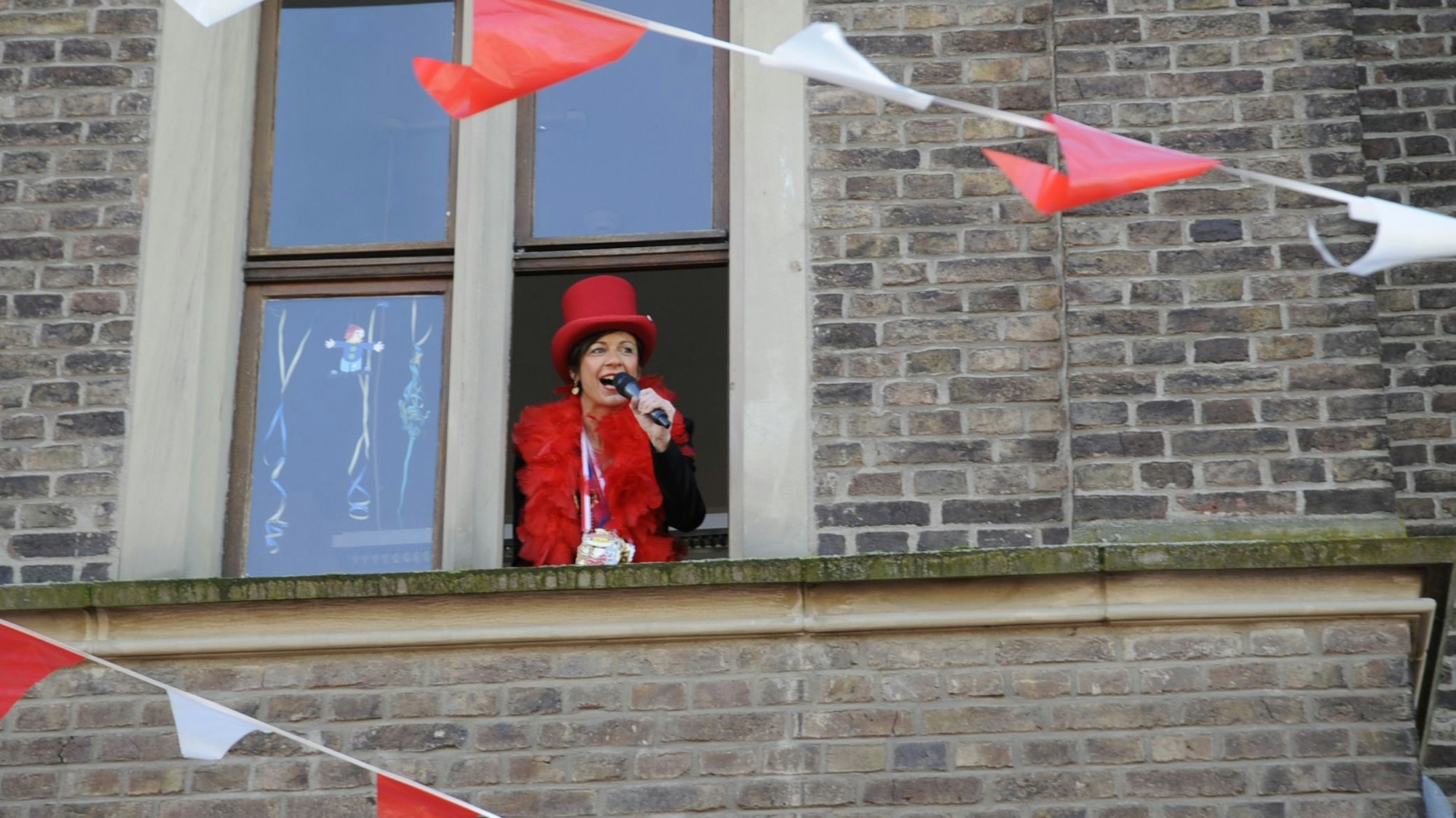 Eine Frau schaut mit einem Mikrofon in der Hand aus einem Fenster.