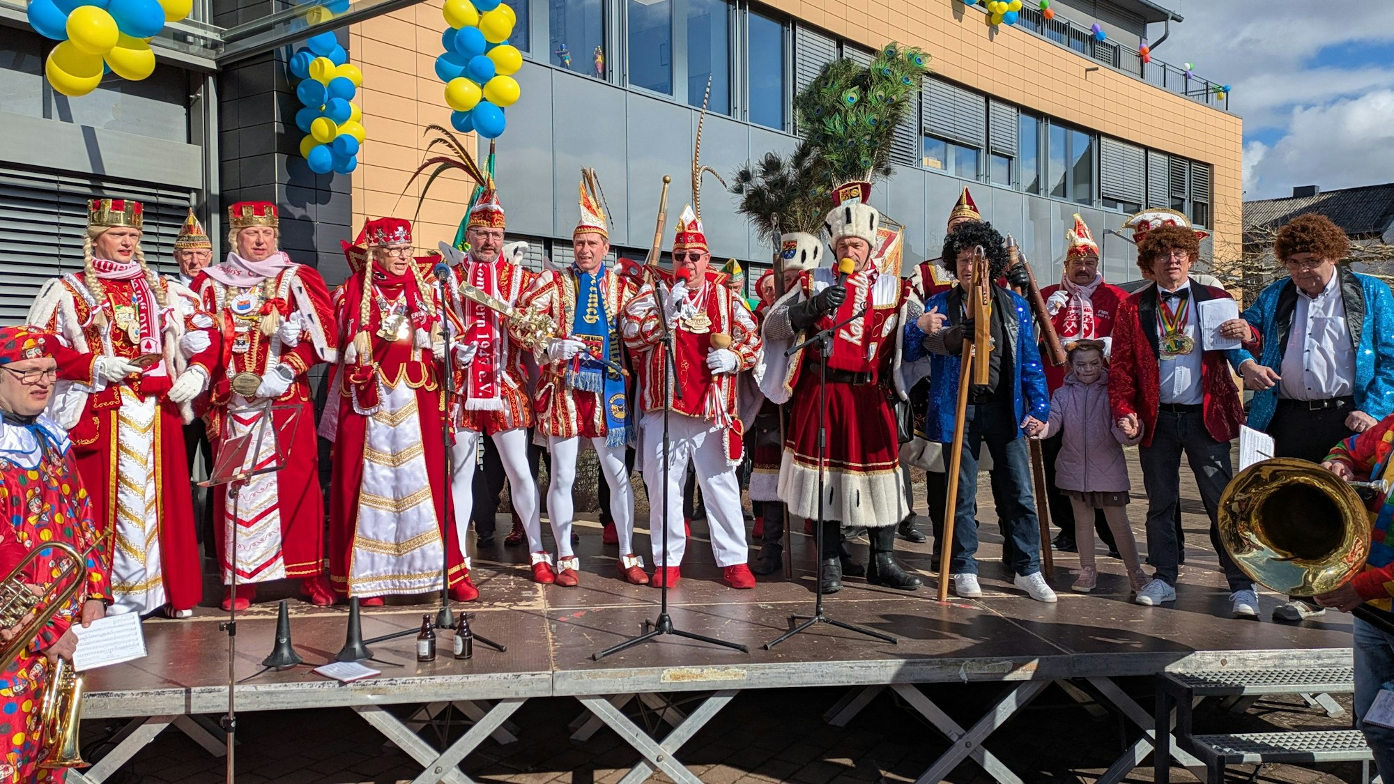 Rot-weiße Kostüme haben die Dreigestirne der Stadt Mechernich. Sie stehen auf der Bühne vor dem Rathaus.