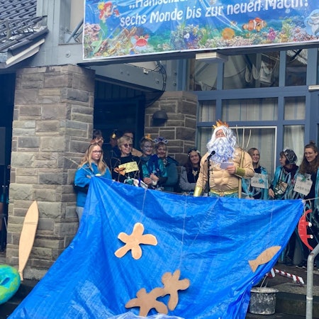 Kürtens Bürgermeister Willi Heider steht im Poseidon-Kostüm vor den Rathaus-Mitarbeitern, die als blaue aquatische Fabelwesen verkleidet sind.