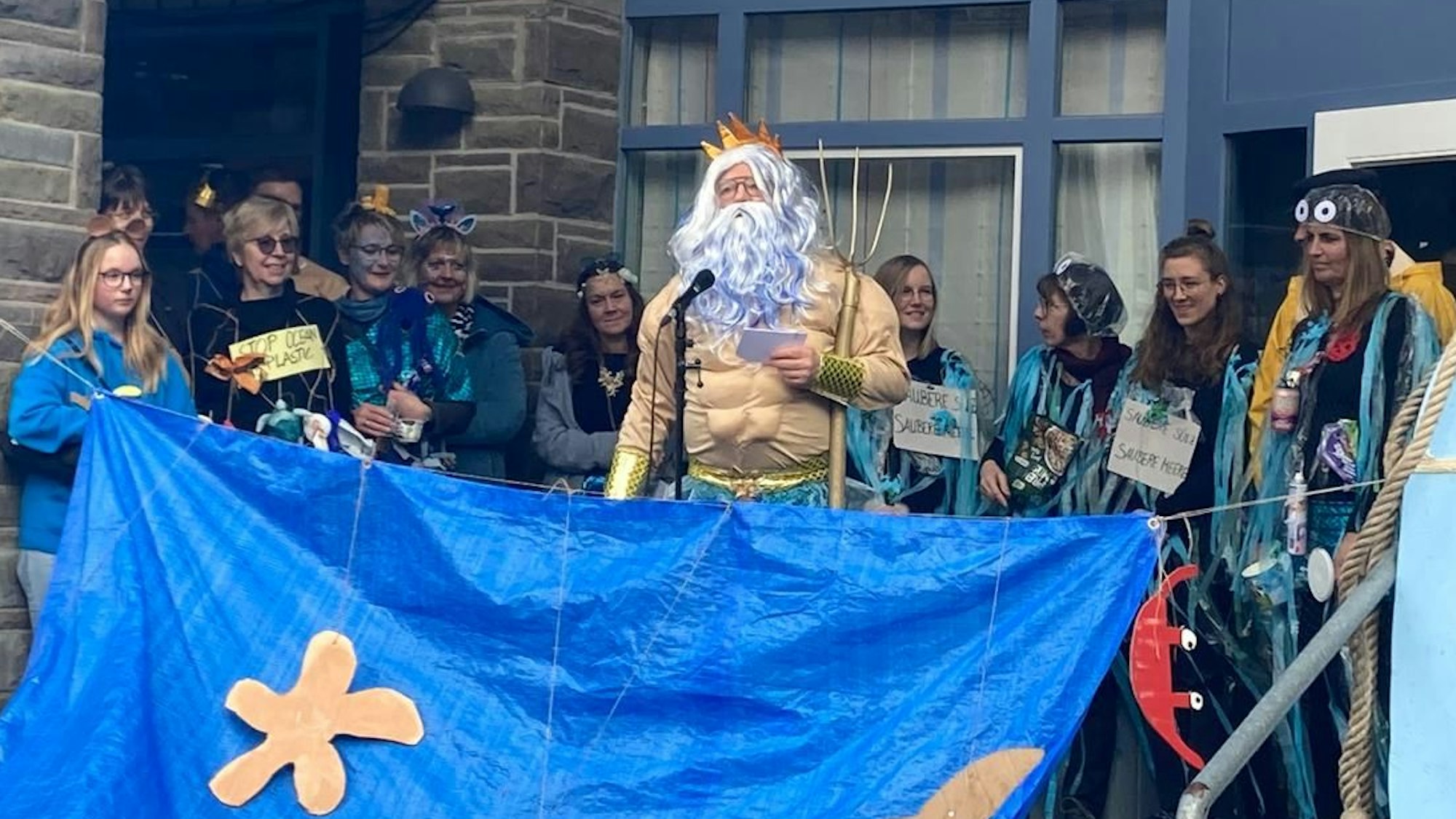 Kürtens Bürgermeister Willi Heider steht im Poseidon-Kostüm vor den Rathaus-Mitarbeitern, die als blaue aquatische Fabelwesen verkleidet sind.