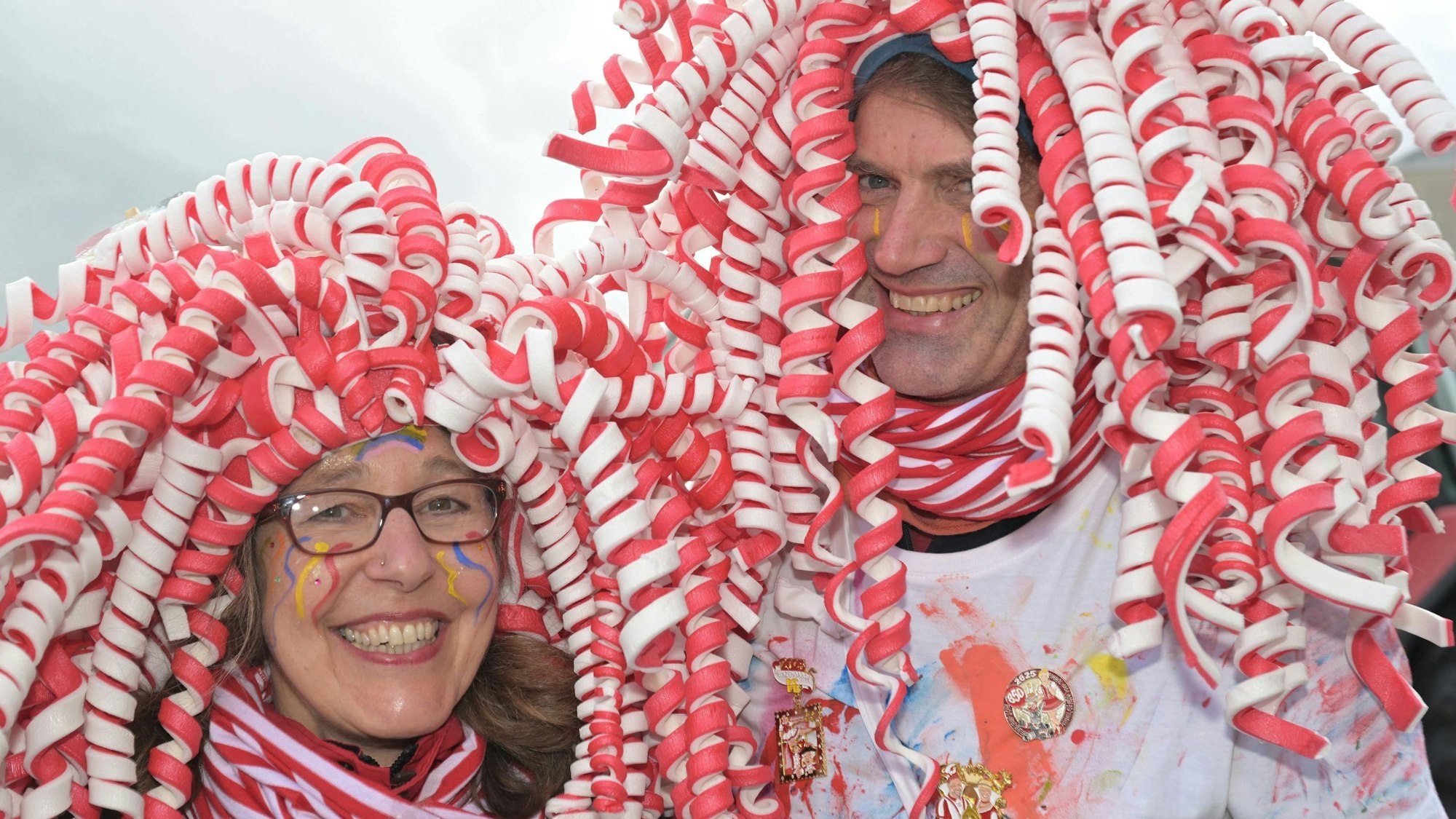 Eine Frau und ein Mann im Malerkostüm mit rot-weißer Perücke lachen in die Kamera.