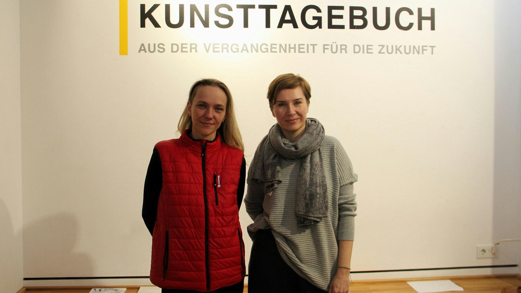 Zwei Frauen stehen vor einer Wand, auf der in großen Lettern Ukrainisches Kunsttagebuch steht
