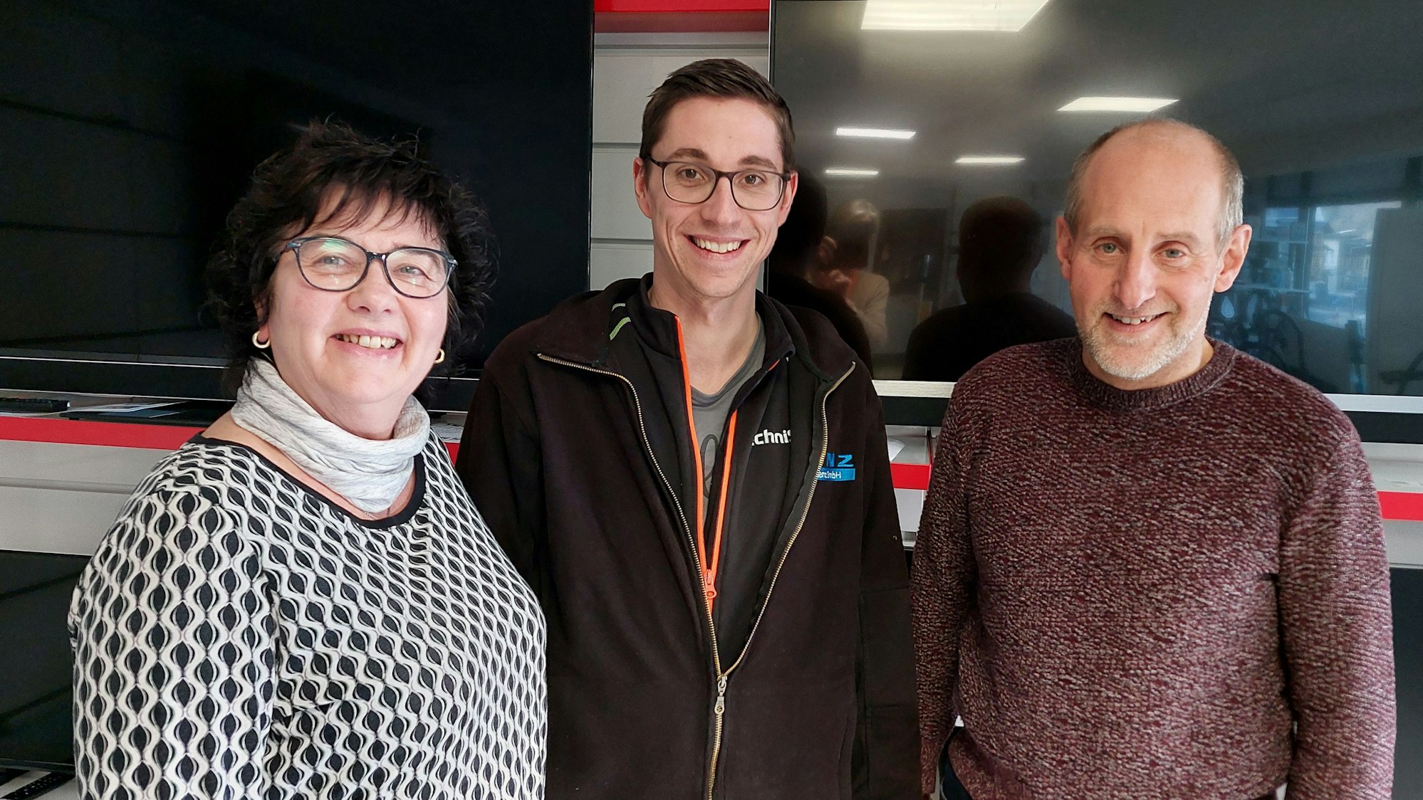 Zwei Männer und eine Frau stehen in einem Geschäft vor ausgestellten Fernsehern in einem Geschäft.
