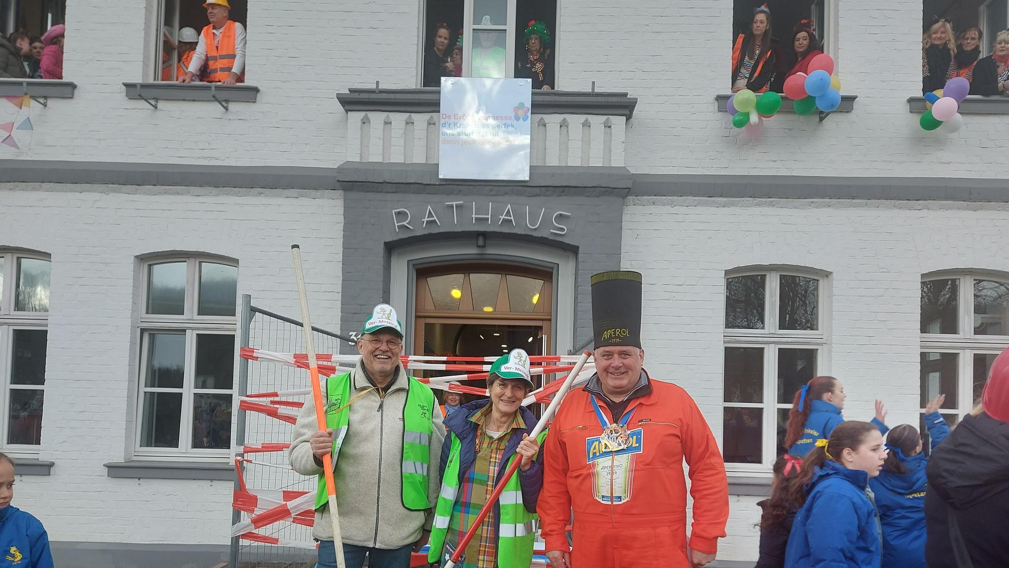 Drei Menschen stehen vor einem Rathaus.