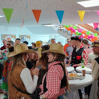 Auf dem Bild sind zahlreiche kostümierte Menschen zu sehen, die um Stehtischen herum stehen.