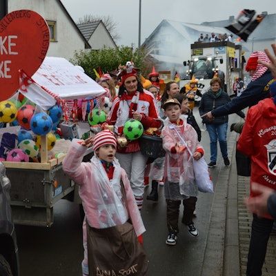 Zahlreiche kostümierte Karnevalisten beteiligen sich am Zug in Kall-Wahlen. Auf einem Anhänger haben sie ein rotes Herz mit der Aufschrift „jecke Ecke“ befestigt.