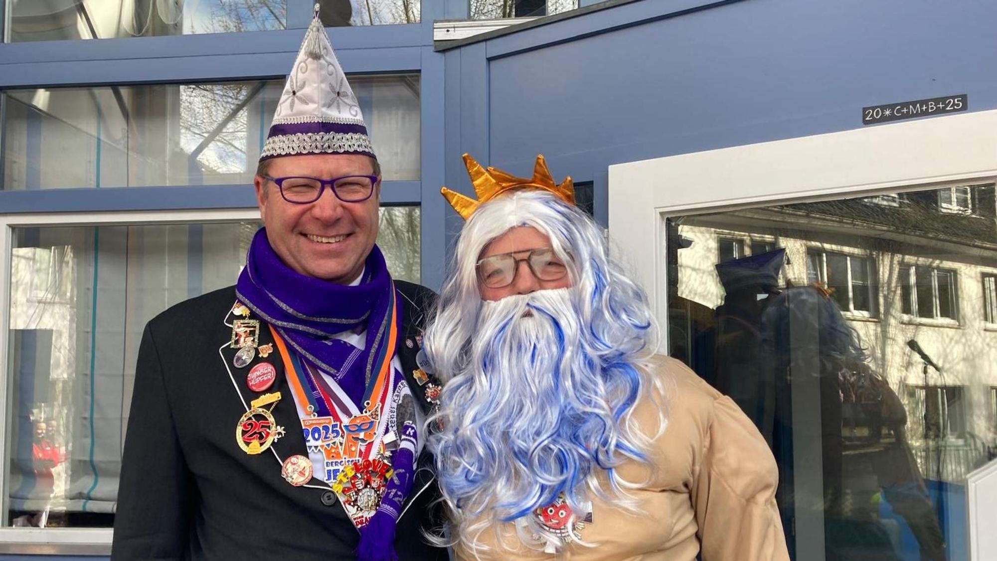 Im Poseidon-Kostüm steht Willi Heider neben Thorsten Kurpjuhn vom Kürtener Karnevalsverein, der einen weißen Hut und einen lilafarbenen Schal trägt.