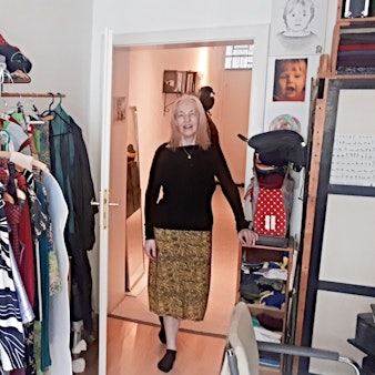 Eine Frau in Rock und schwarzem Oberteil steht in der geöffneten Tür zu ihrem Atelier.