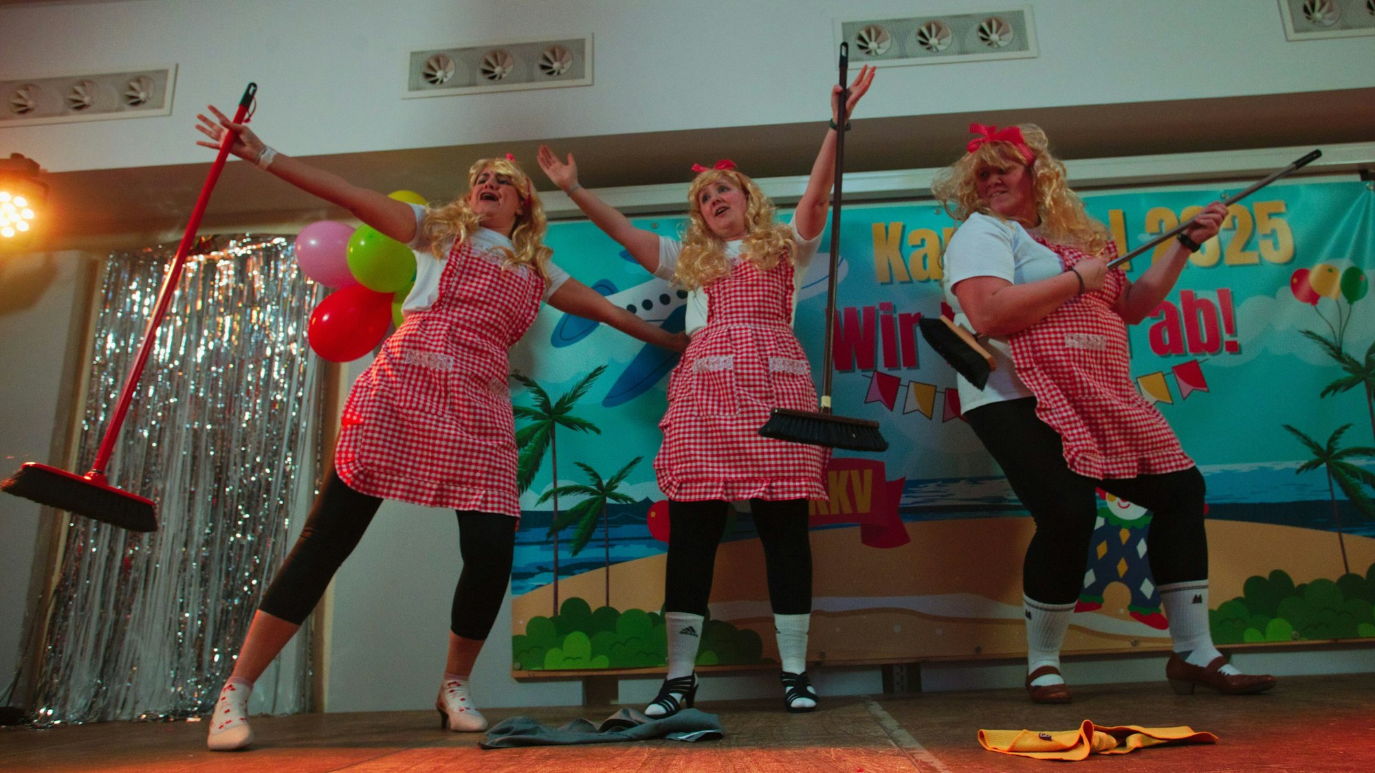 Drei Frauen, die als Reinigungskräfte verkleidet sind, tanzen auf der Bühne.