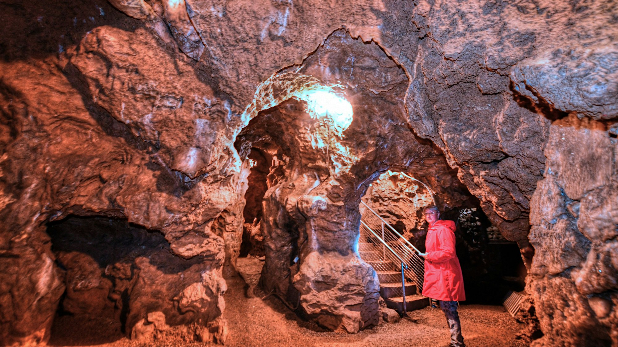 In einer Tropfsteinhöhle steht eine Frau in einem roten Regenmantel.