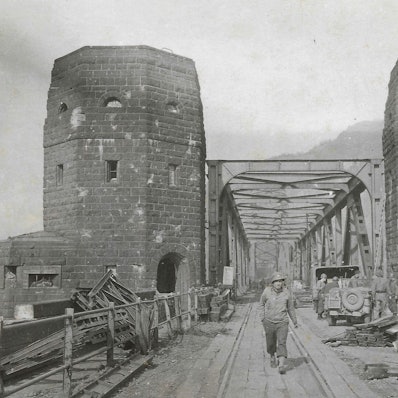 Eine historische Aufnahme, auf der ein Soldat zwischen den Türmen der Brücke von Remagen hindurch geht.