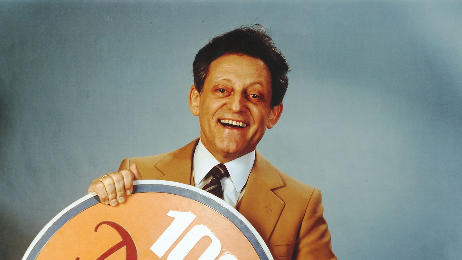 Hans Rosenthal hält in den 197er Jahren ein Schild in den Armen zur 100. Ausgabe von "Dalli Dalli"