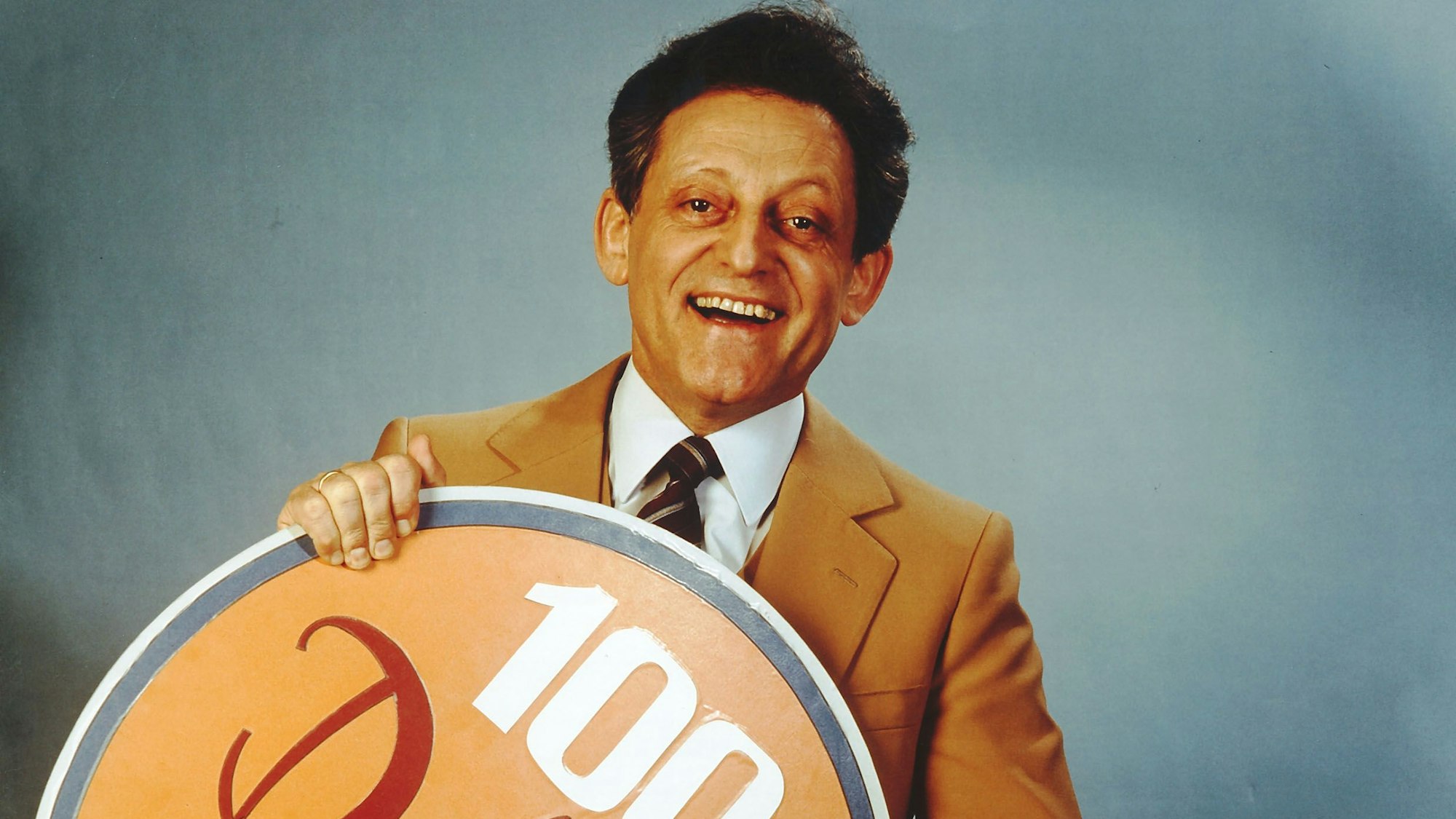 Hans Rosenthal hält in den 197er Jahren ein Schild in den Armen zur 100. Ausgabe von "Dalli Dalli"