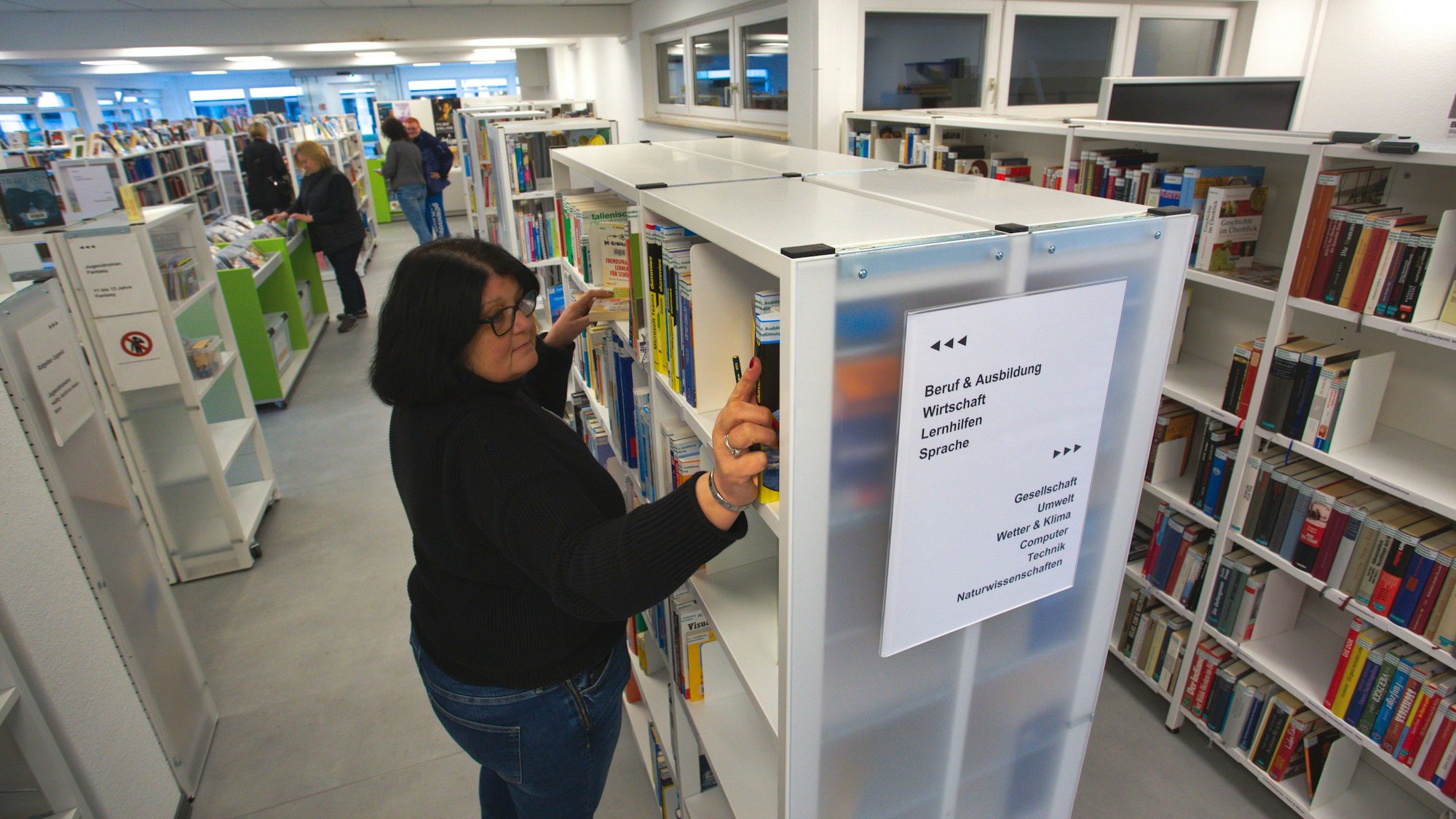 Eine Frau sortiert Bücher in ein Regal in einer Stadtbibliothek ein.