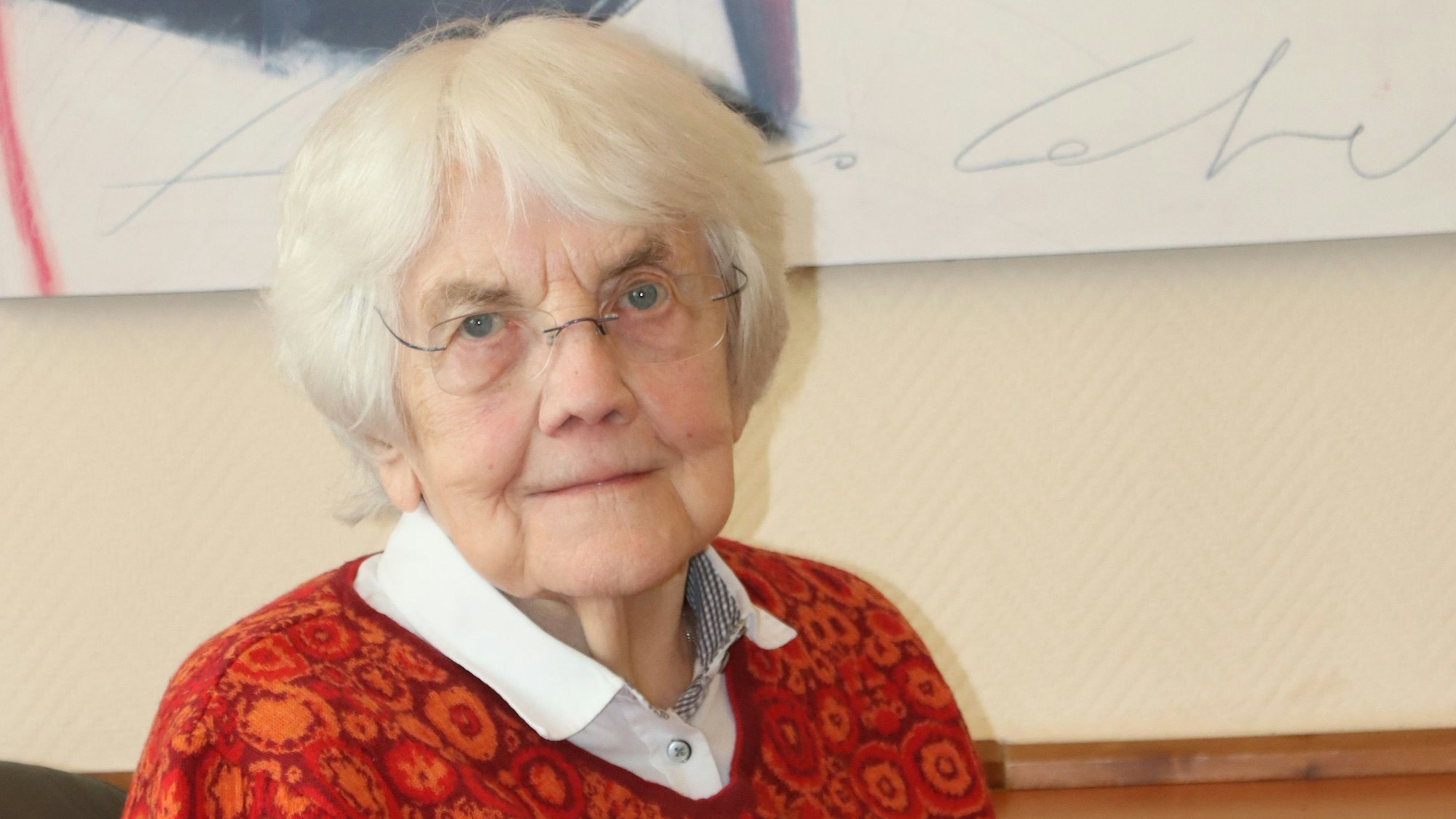 Mario Dickopf hat weißes Haar, blaue Augen und trägt eine Brille. Sie trägt einen roten Pullover mit Blumenmuster und darunter ein weißes Hemd.