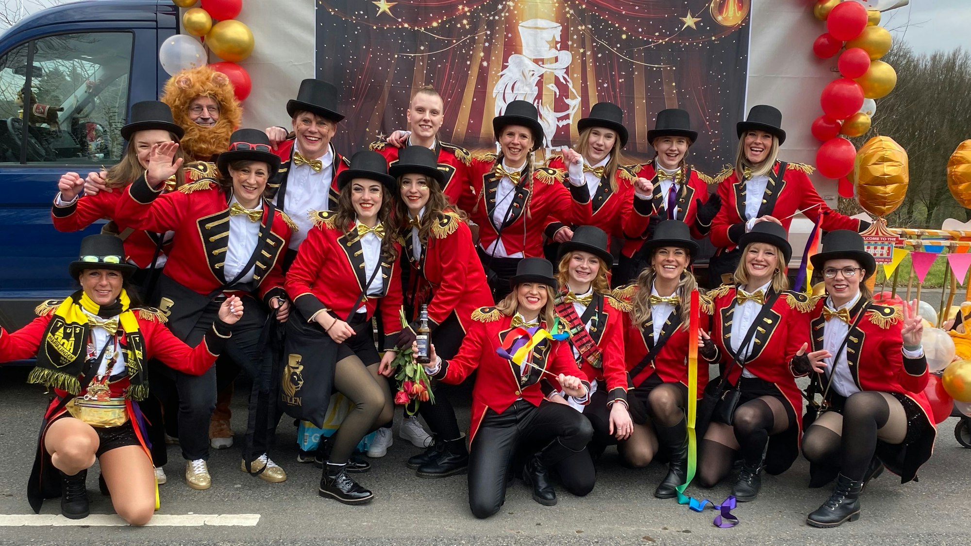 Frauen in Domteursfräcken hocken und stehen vor einem Wagen.