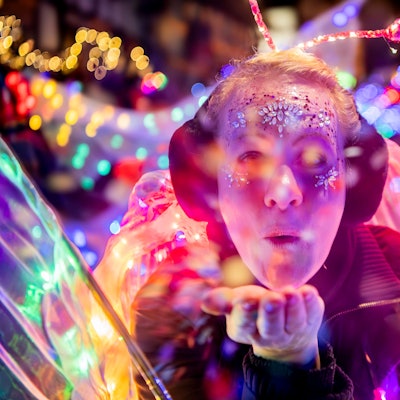 Das Bild zeigt eine Teilnehmerin des Lichterzugs. Sie pustet Konfetti in Richtung Kamera.