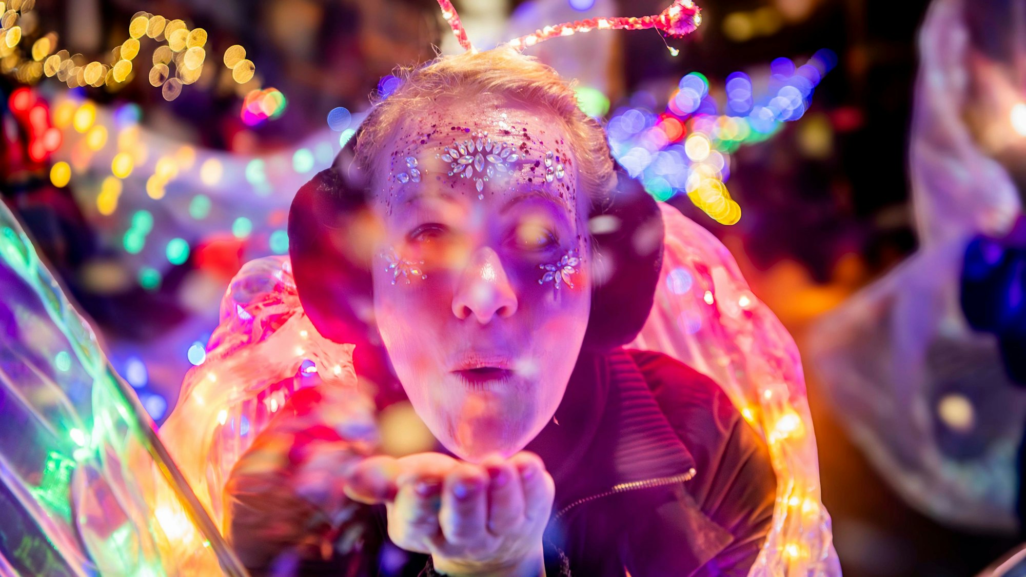 Das Bild zeigt eine Teilnehmerin des Lichterzugs. Sie pustet Konfetti in Richtung Kamera.