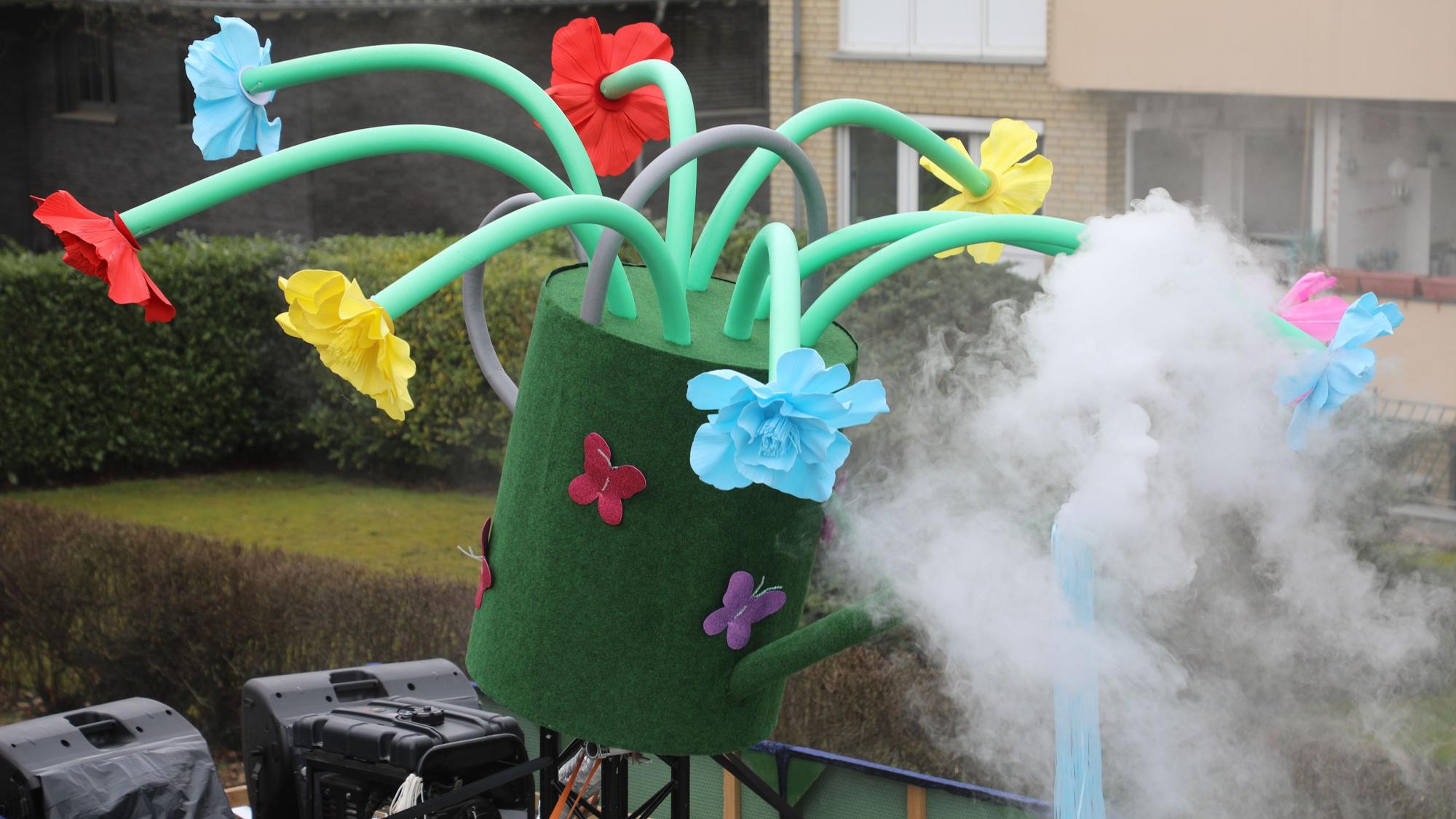 Auf einer Gießkanne mit Blumen qualmt es.