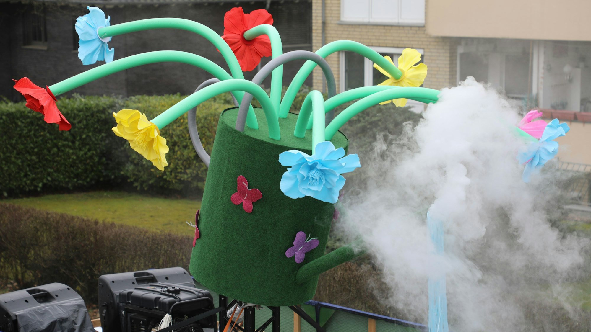 Auf einer Gießkanne mit Blumen qualmt es.