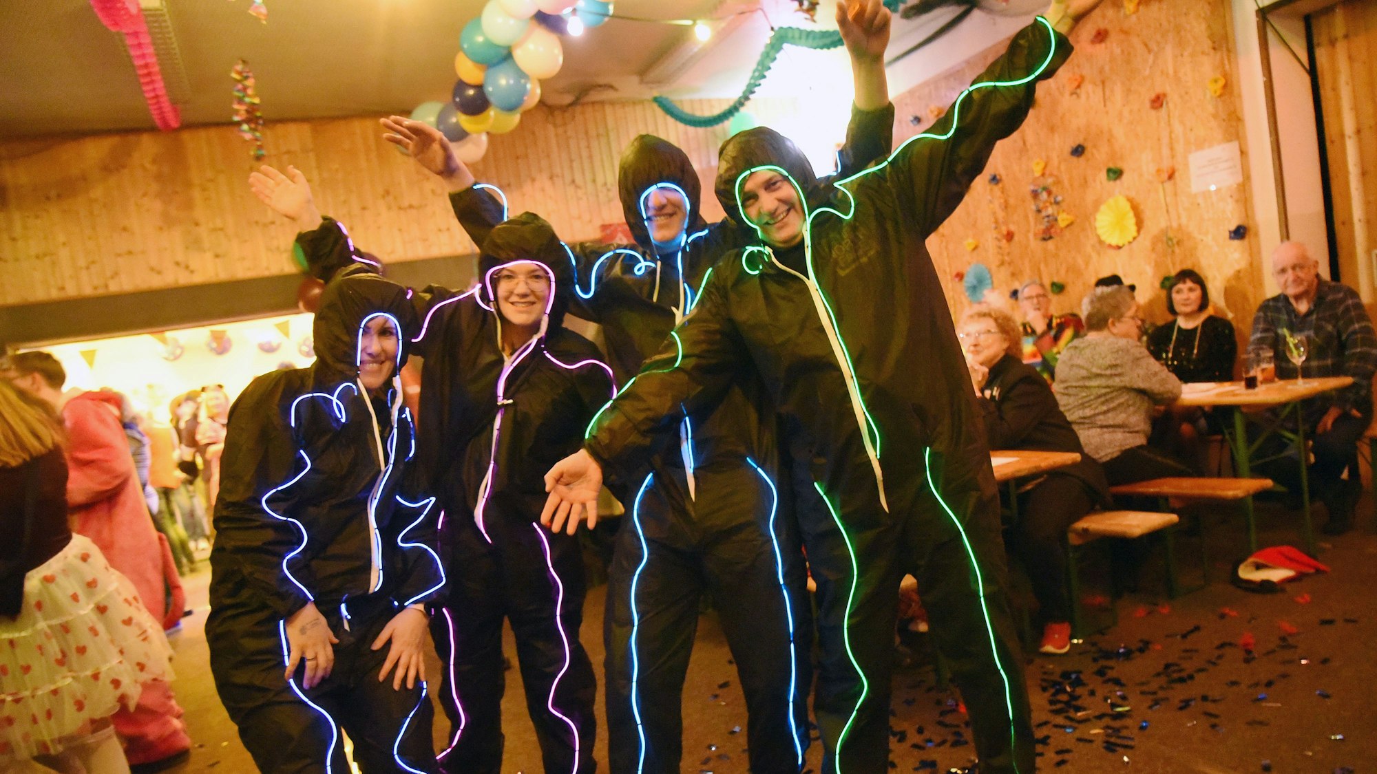 Eine Gruppe in schwarzen Kostümen mit neonfarbenen und leuchtenden Mustern.