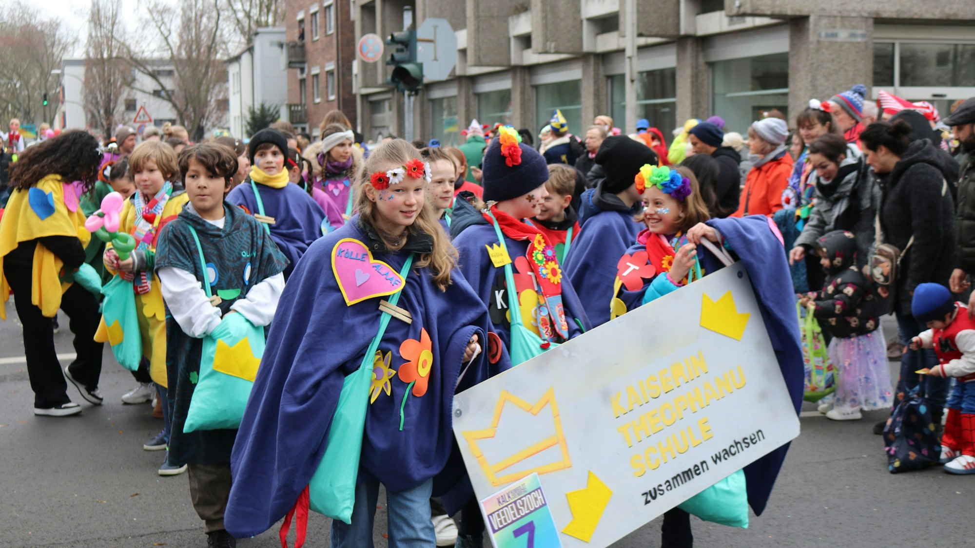 Eine Gruppe Kinder läuft verkleidet mit blauen Umhängen und Herzen darauf durch das Veedel.