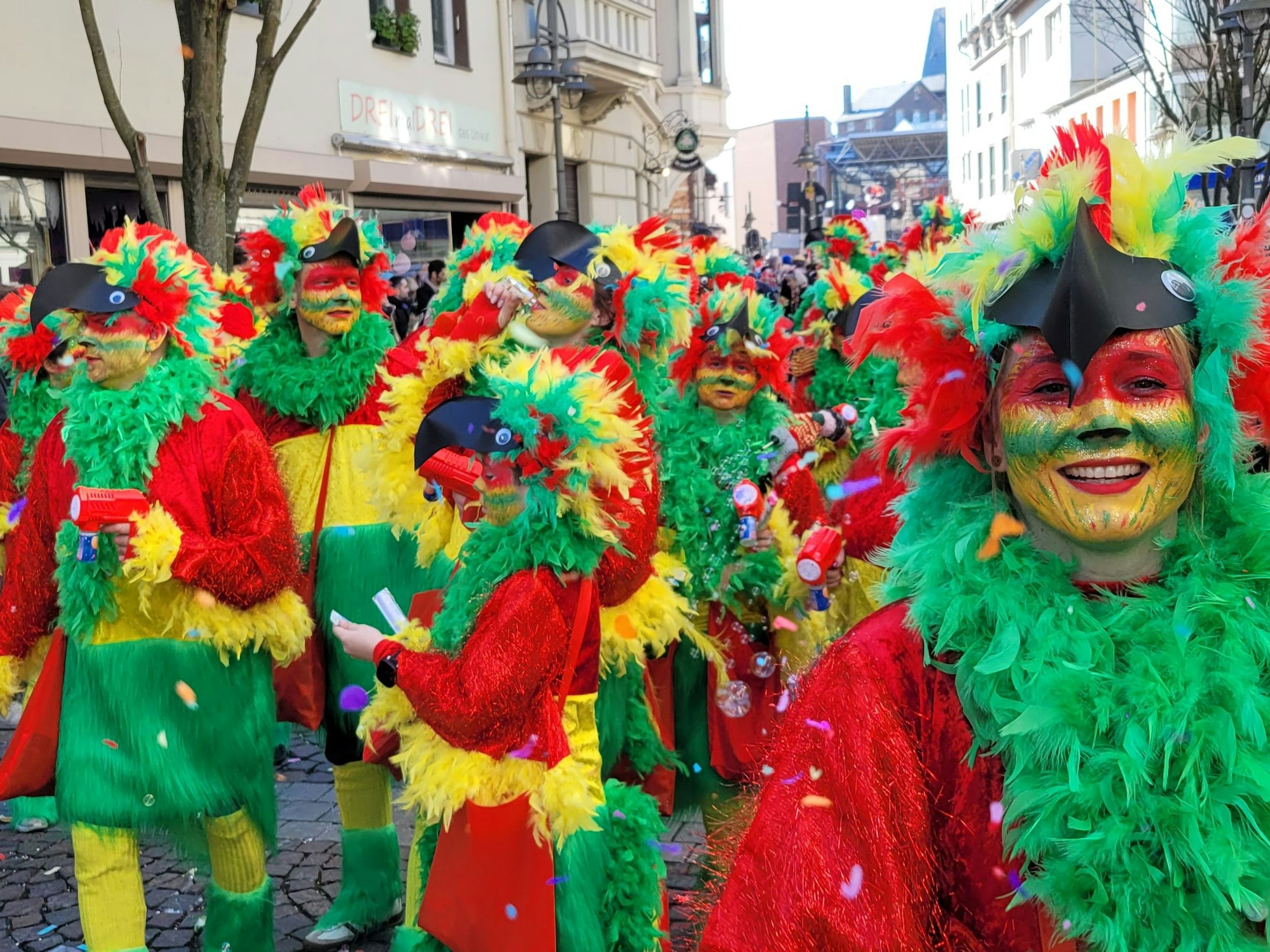Rot, Gelb und Grün: Kinder und Erwachsene in Papageienkostümen.
