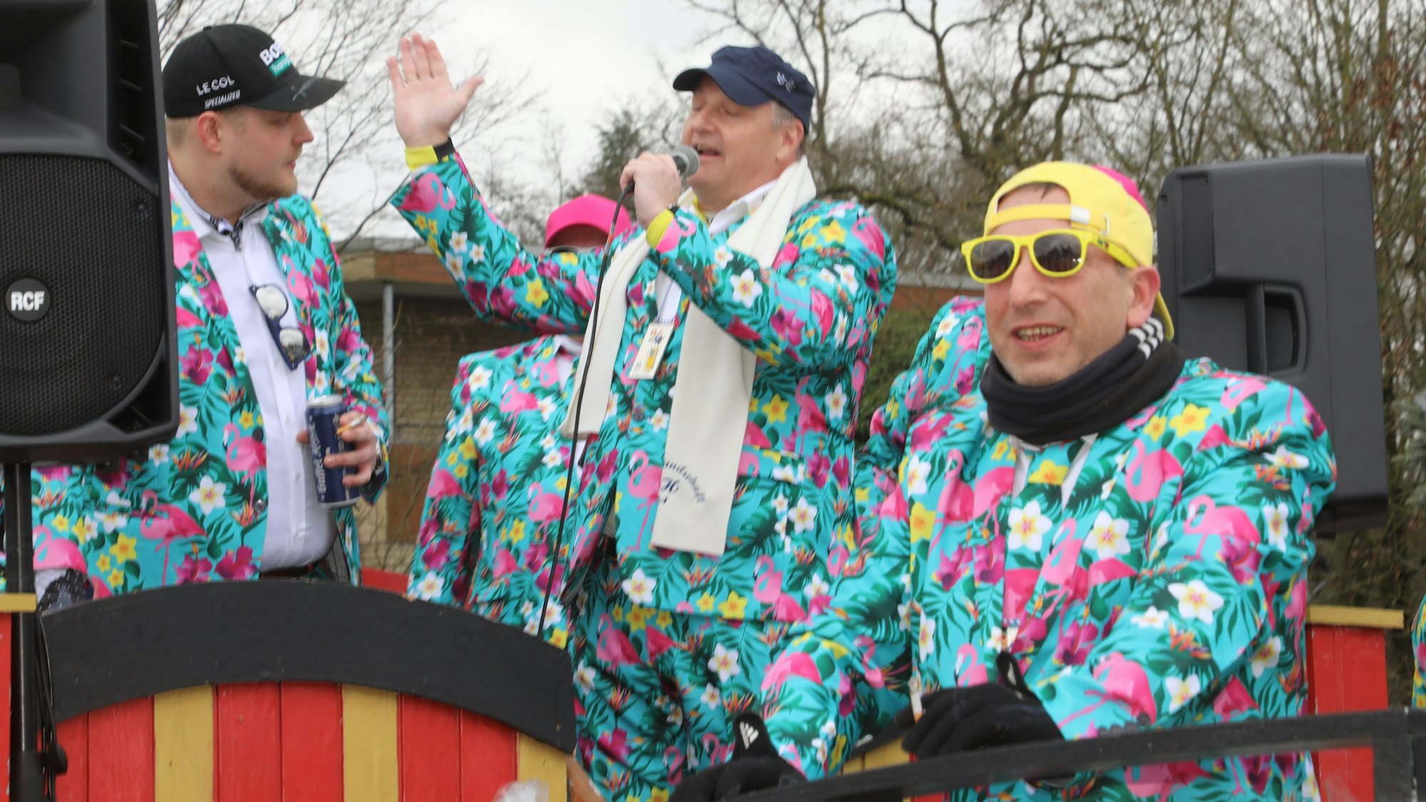 Männer in Blumen-Flamingo-Anzügen stehen auf einem Wagen.