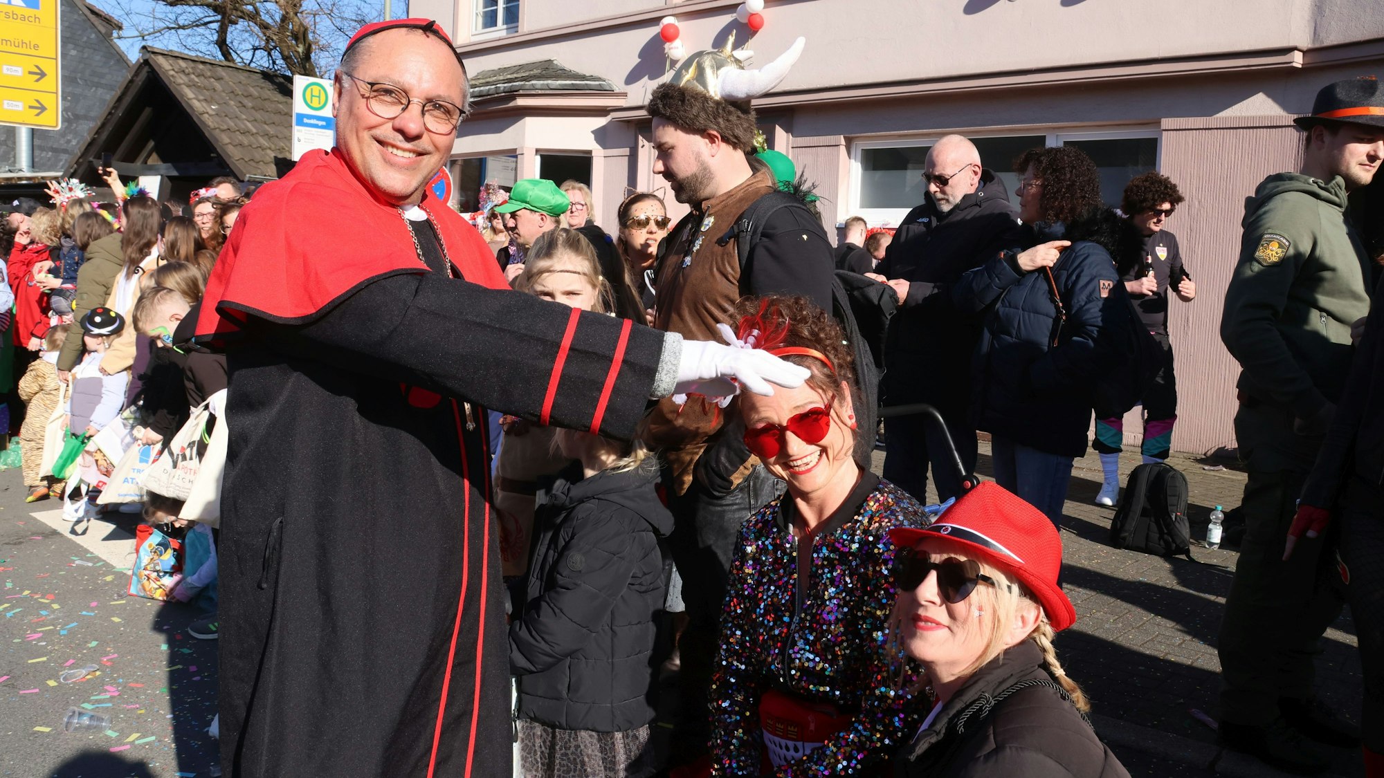 Ein als Bischof verkleideter Mann spendet zwei kostümierten Frauen Segen.
